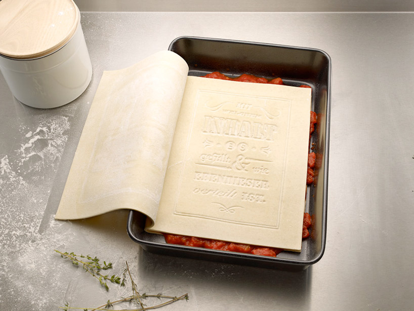 Book made of pasta in pan with first layer of lasagna ingredients