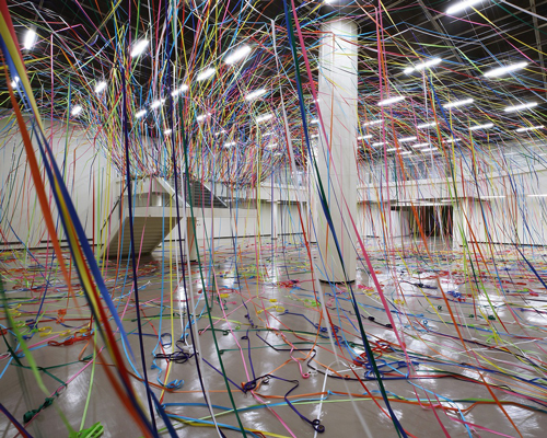 meticulous fishing line grids trace the falling orbits of colorful paper rolls