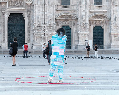 man wrapped by face masks struggles to move in 'no escape' performance in milan, italy