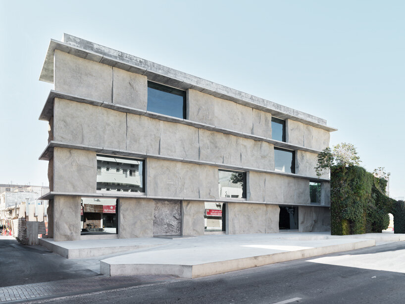 sand-casted concrete façade clads the  green corner building by anne holtrop in bahrain