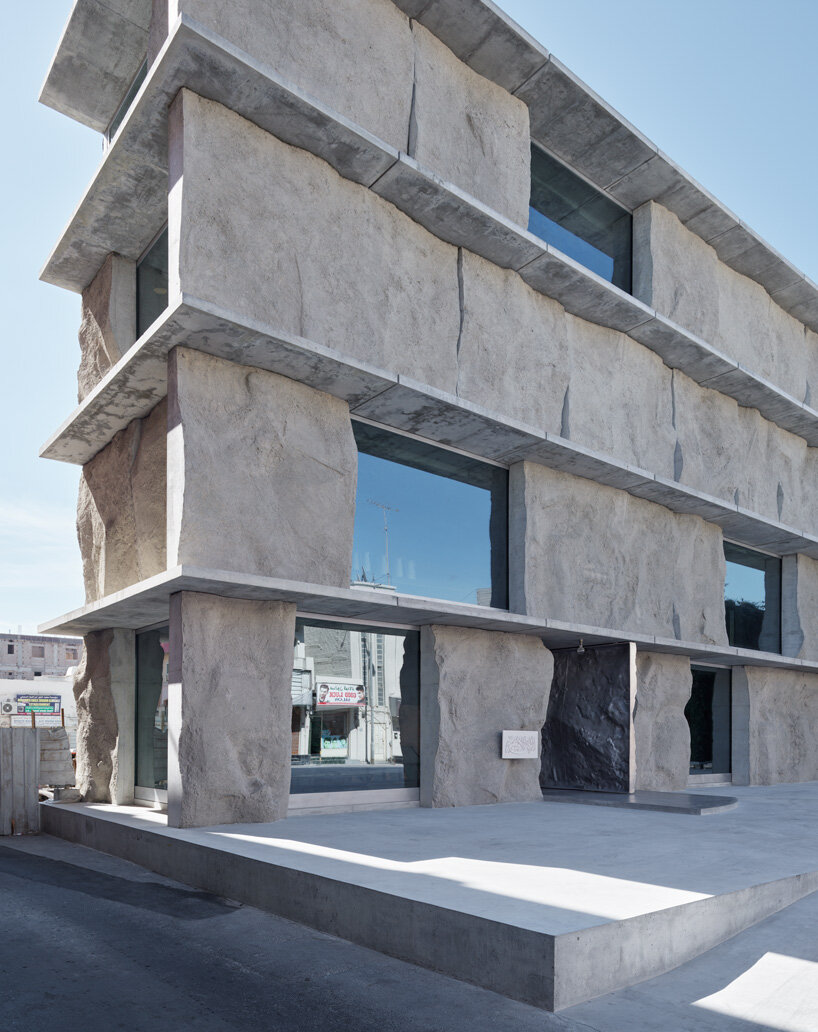 sand-casted concrete façade clads the  green corner building by anne holtrop in bahrain