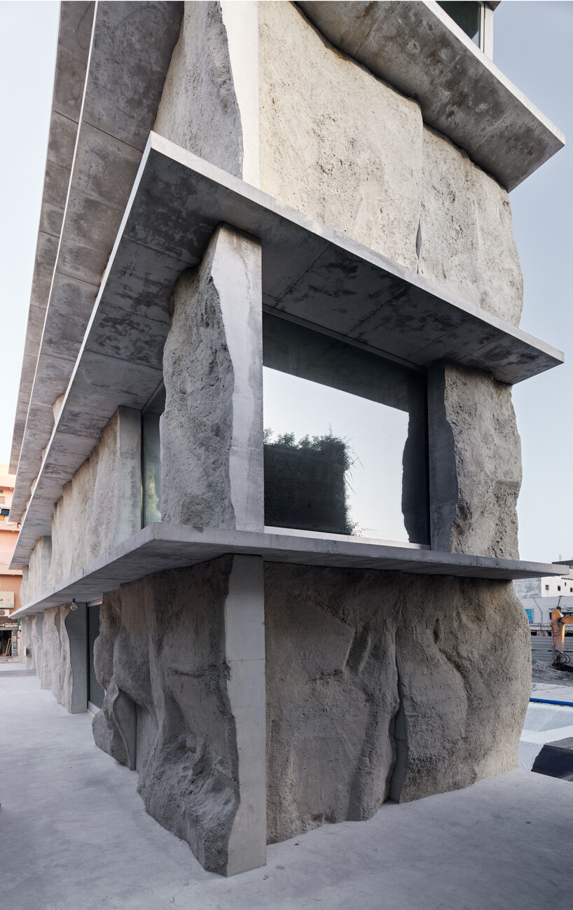 sand-casted concrete façade clads the  green corner building by anne holtrop in bahrain