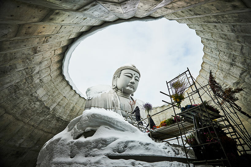 beneath tadao ando’s hill, azuma makoto installs flower bouquet into arms of the buddha