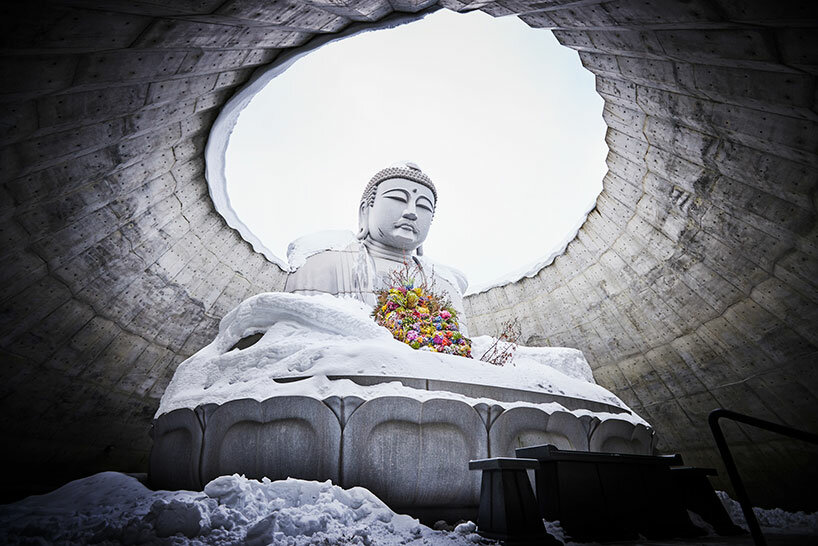 beneath tadao ando’s hill, azuma makoto installs flower bouquet into arms of the buddha