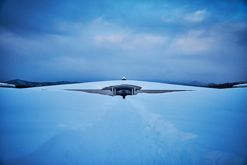 beneath tadao ando’s hill, azuma makoto installs flower bouquet into arms of the buddha