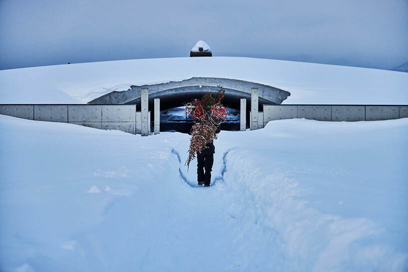 beneath tadao ando’s hill, azuma makoto installs flower bouquet into arms of the buddha