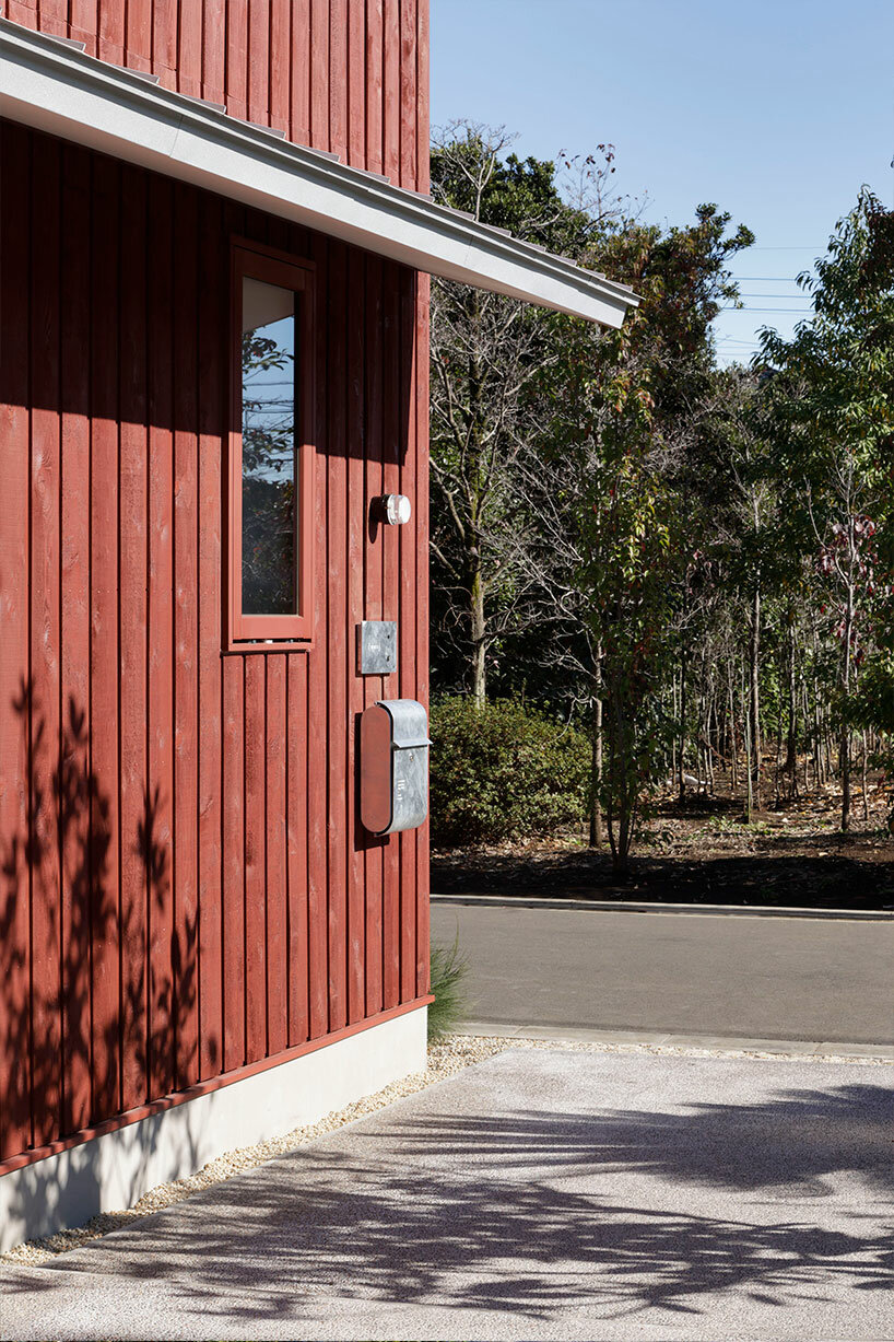 topped with a silver roof, deep red exterior clads wooden house in tokyo