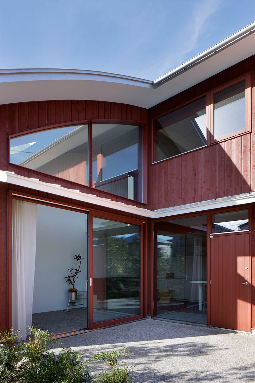 topped with a silver roof, deep red exterior clads wooden house in tokyo