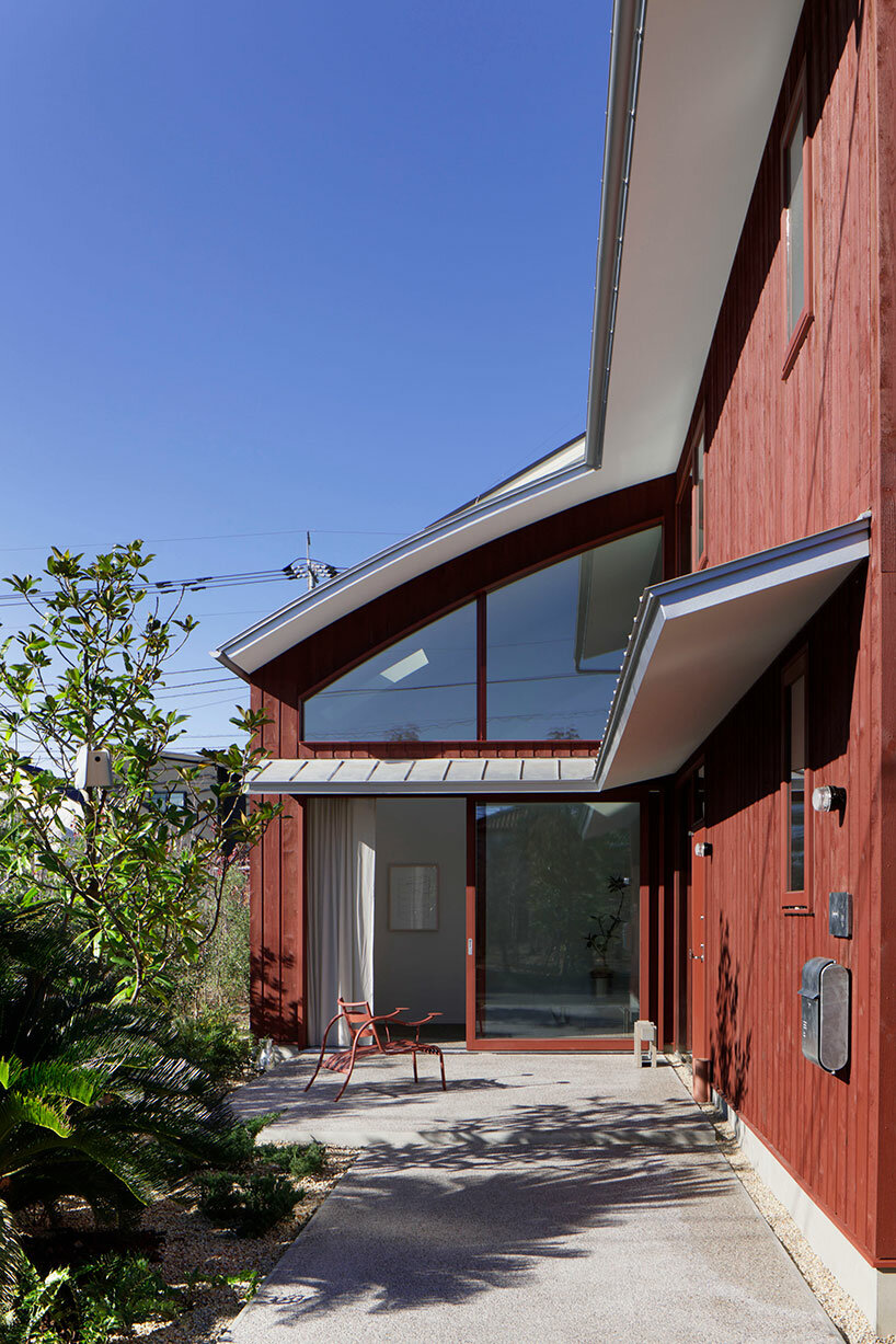 topped with a silver roof, deep red exterior clads wooden house in tokyo