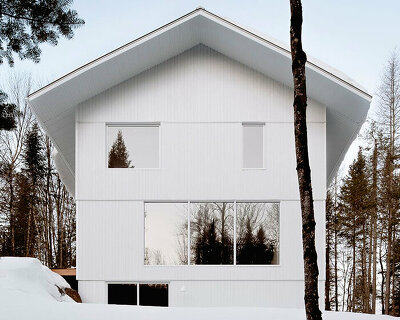 white wooden residence melds with the snowy landscape of quebec's forest