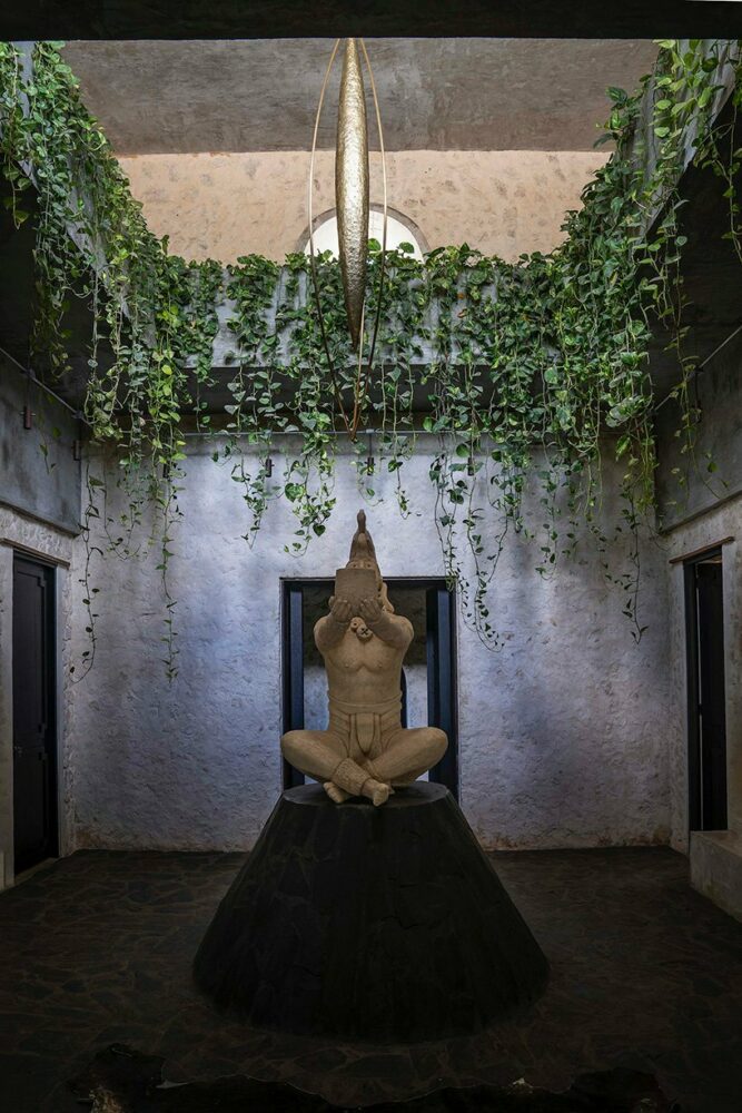 a statue of a seated man raises his hands in gratitude generating tension towards the installation