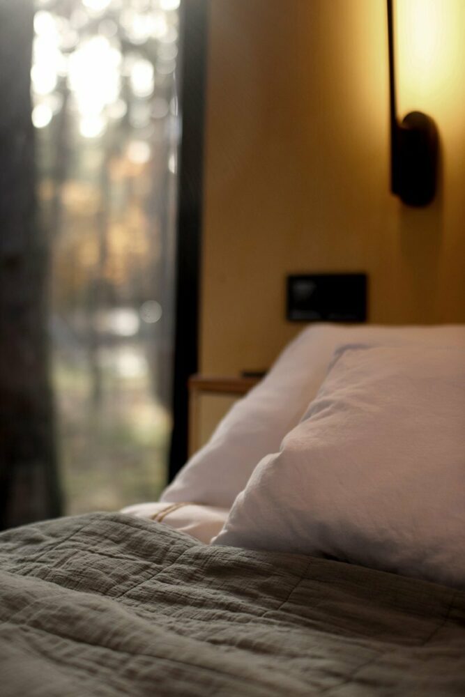 the grand bed stands next to a large forest-facing window