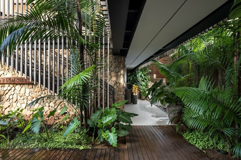 the material palette includes natural stone at the base, a dark green metal structure, and cladding panels