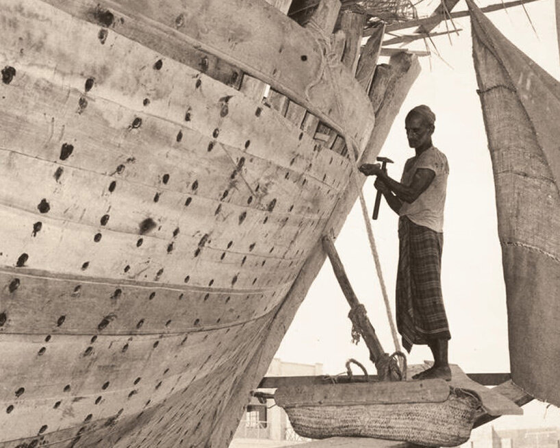 a man works on a large wooden boat (dhow) at a shipyard in Manama in about 1950 | image courtesy the National Pavilion of the Kingdom of Bahrain