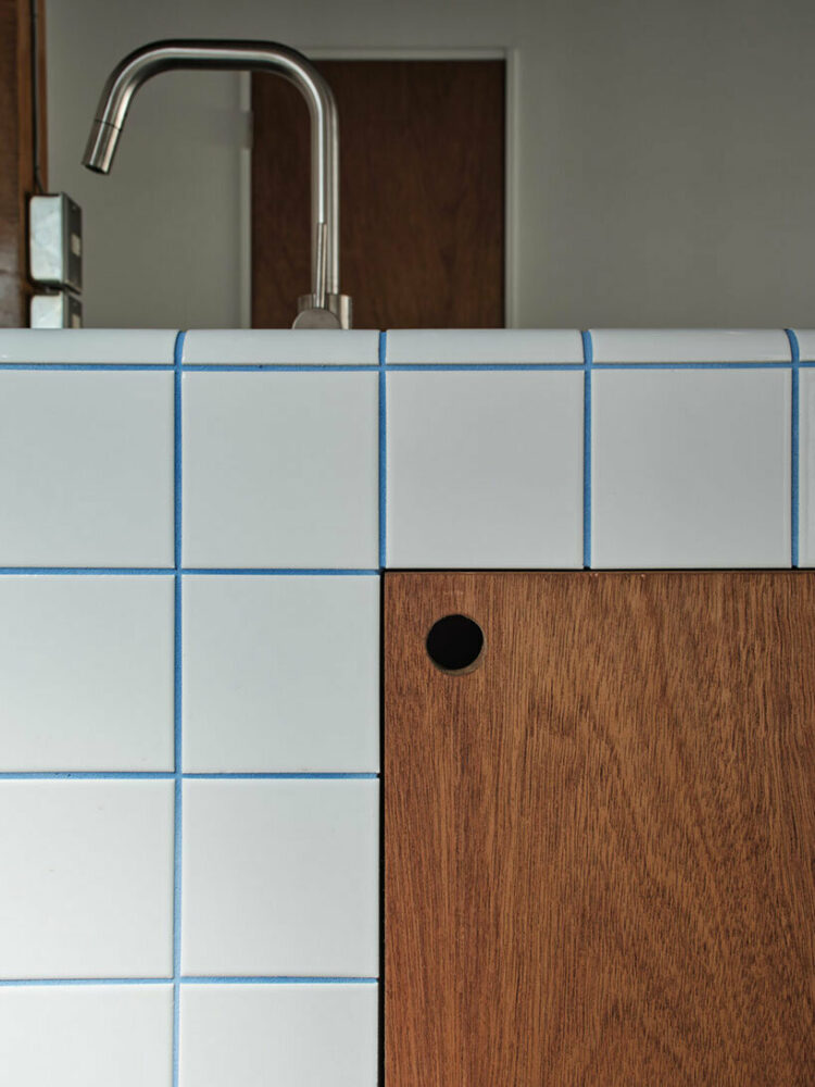 a modern square-shaped white tile kitchen counter with blue grout lines adorns the renovated residence