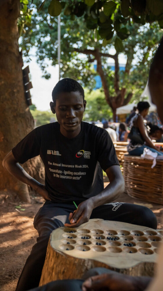 a man teaching others how to play omweso on the mweso log | image by Brian Musinguzi