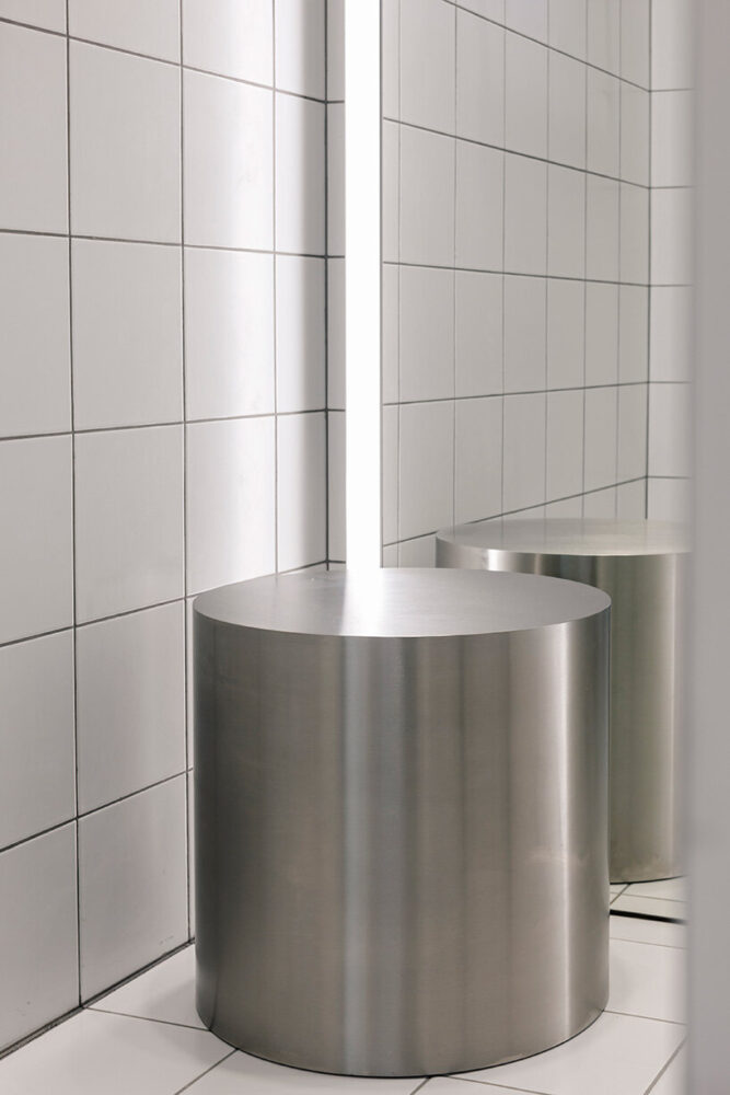 sleek fitting rooms combine white tiles with round metallic stools