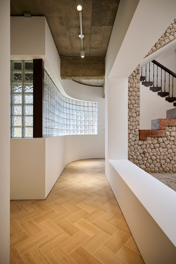 tiled glass windows, exposed beams, staircases, and textured stone walls compose the residence