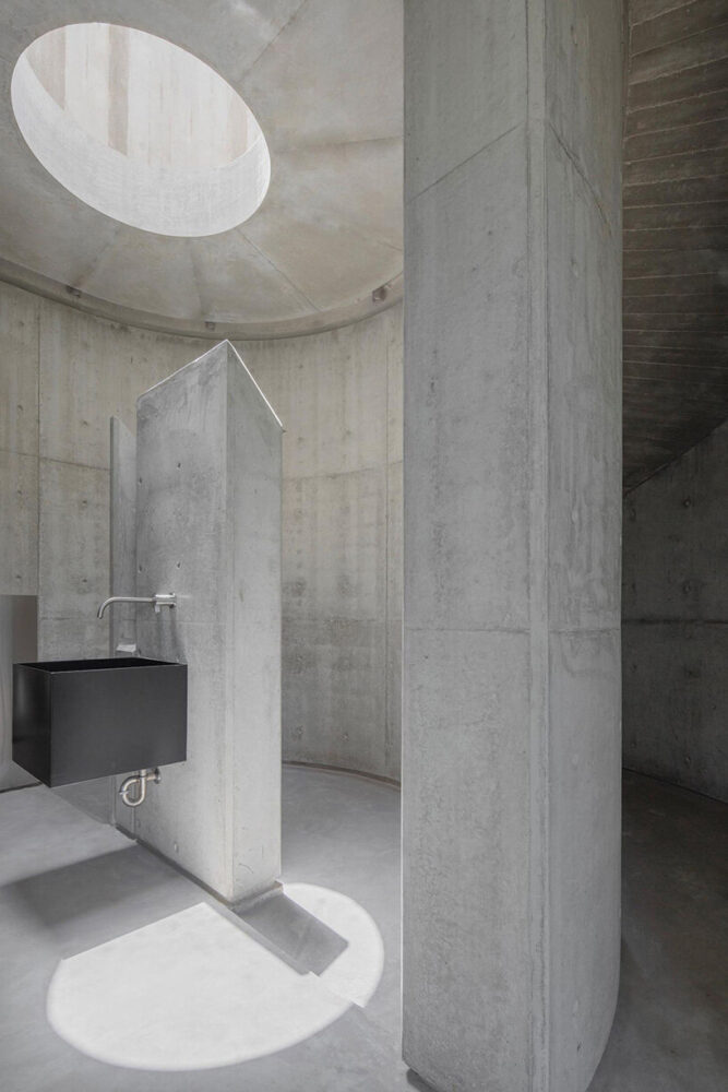 the skylit shower enclosed by the curved bathroom partition continues the interplay between mass and light