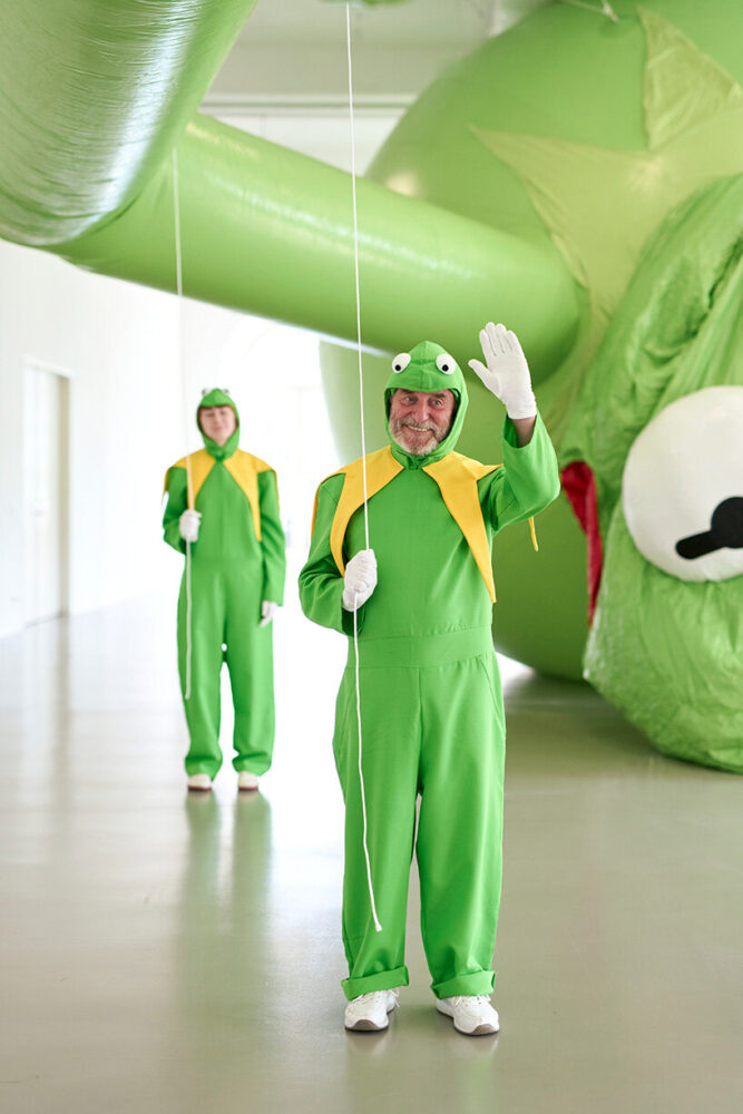 a group of smiling performers dressed as Kermit keep the facade of optimism alive