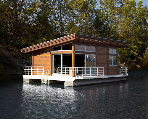 mono-pitch roof shields compact wooden cabin floating along river in serbia