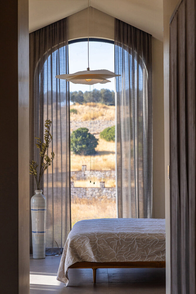 the master bedroom faces the fields, with a tall arched window positioned to capture the landscape