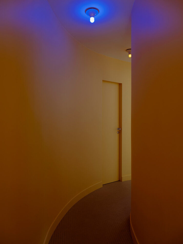 the hallway unfolds as a curved passage illuminated by colored ceiling bulbs