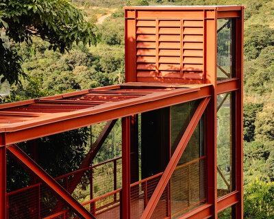 red elevated metal walkway extends casa castela across steep brazilian slope