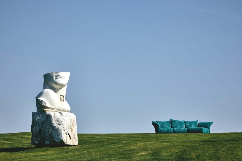 A statue laying over grass with an Edra sofa next to it